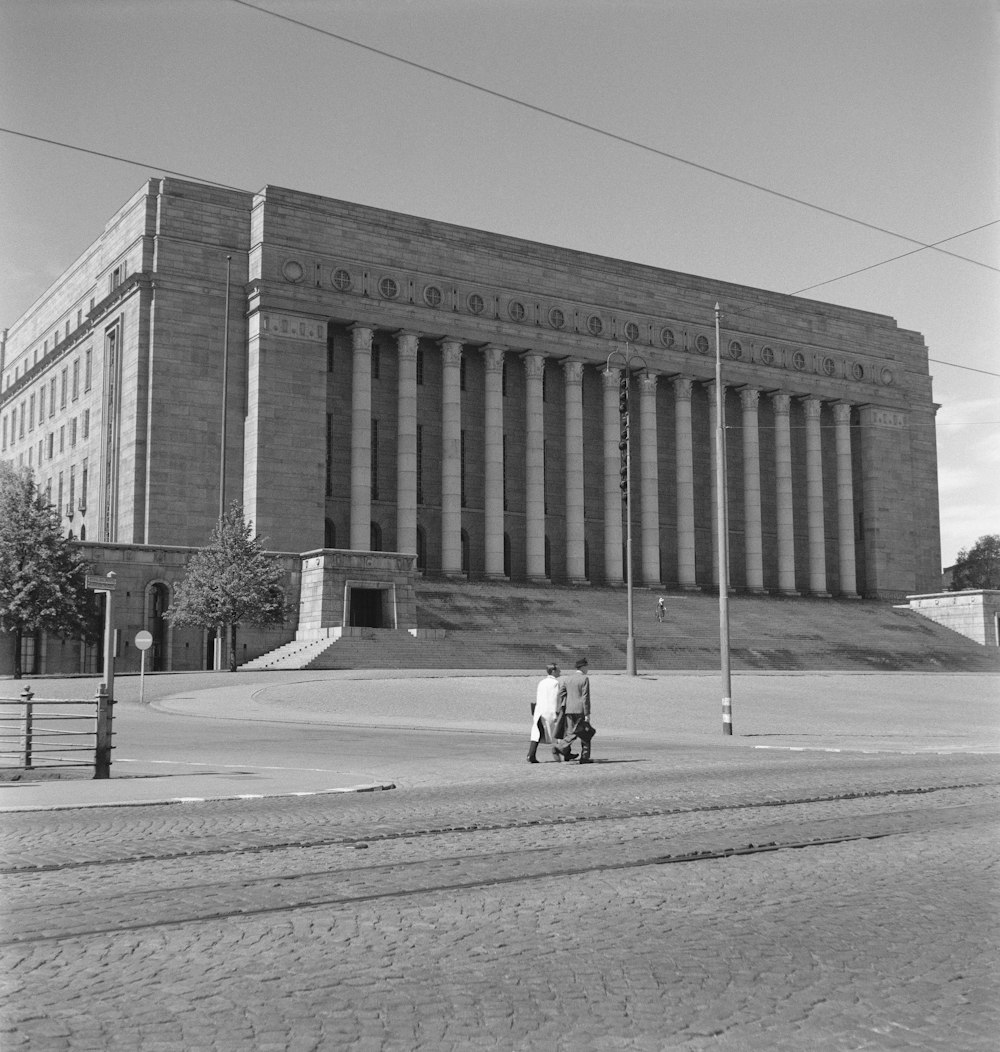 a black and white photo of two people walking in front of a building