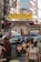 A bustling city street features an archway with a 'Welcome to Manila Chinatown' sign. The area is crowded with cars, motorcycles, and pedestrians. People are engaged in various activities, some wearing masks. The street is lined with buildings, and there are numerous overhead wires.