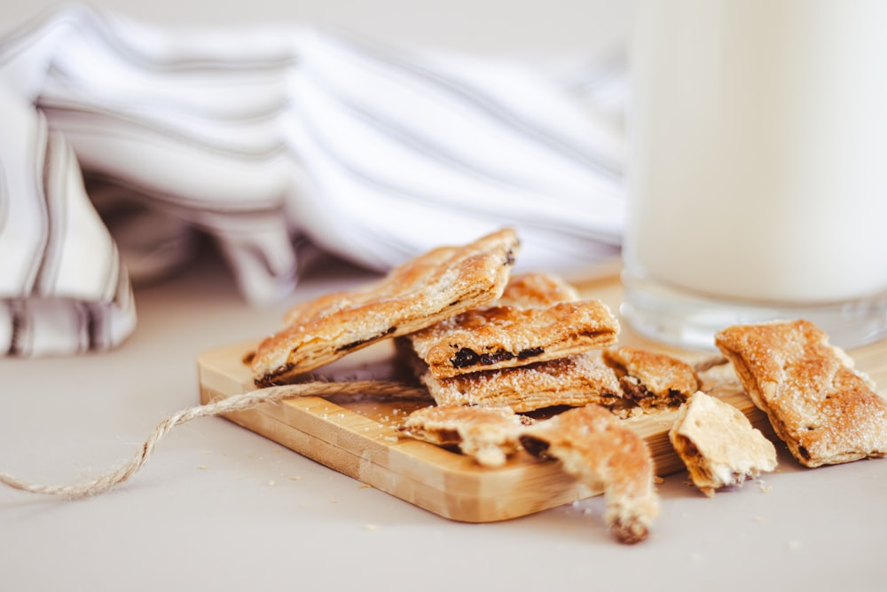 a wooden cutting board topped with crackers next to a glass of milk