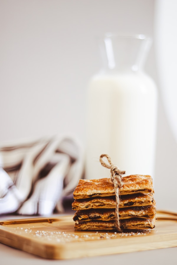 A stack of crackers on a cutting board next to a glass of milk