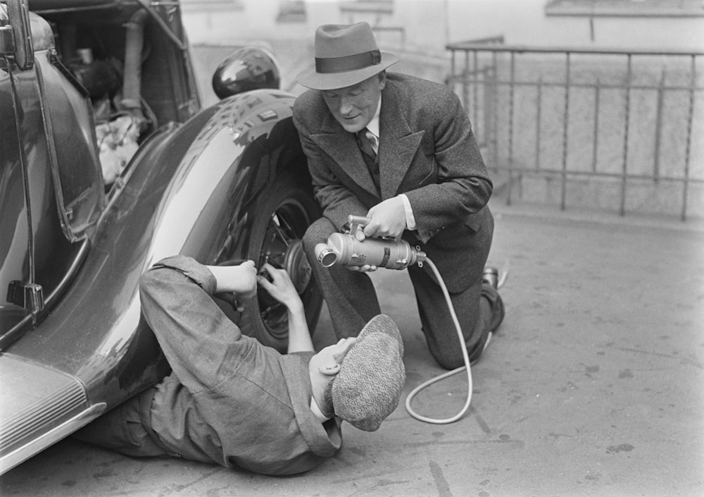 a black and white photo of a man working on a car