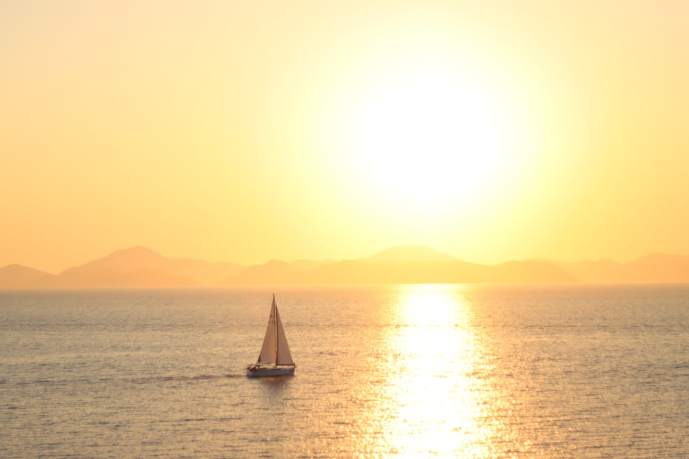 a sailboat in the middle of the ocean at sunset