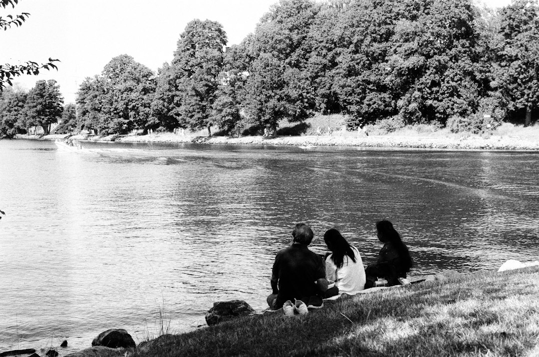 three people sitting on the shore of a lake,