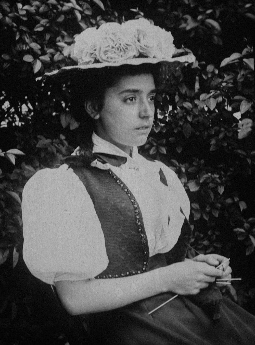 a woman in a dress and hat holding a flower