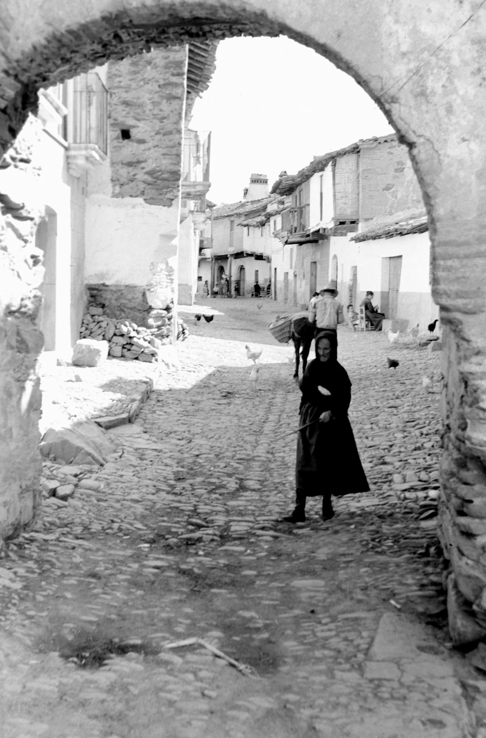 a black and white photo of a woman walking down a cobblestone street