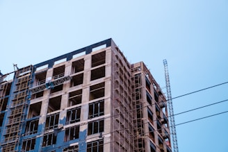Modern commercial building under construction with cranes and scaffolding against a clear sky.