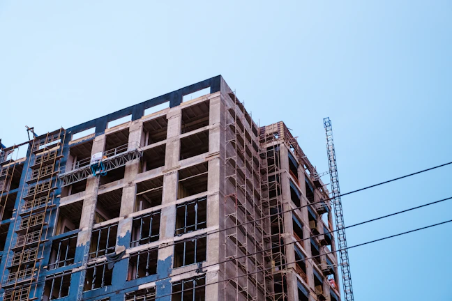 Construction workers assembling a commercial building structure with cranes and scaffolding under a clear blue sky