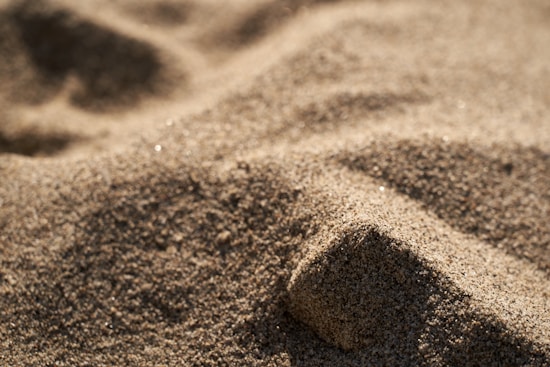 A close-up view of a mound of grainy sand with a soft, sunlit texture and gentle shadows creating depth.