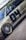 A detailed view of a customized car with prominent wheel rims and a matte finish. The car features decals and sponsor logos, highlighting brands such as BBS and Recaro, with a large number 04 on the side. The vehicle is positioned on a smooth road surface, with greenery visible in the background under a partly cloudy sky.