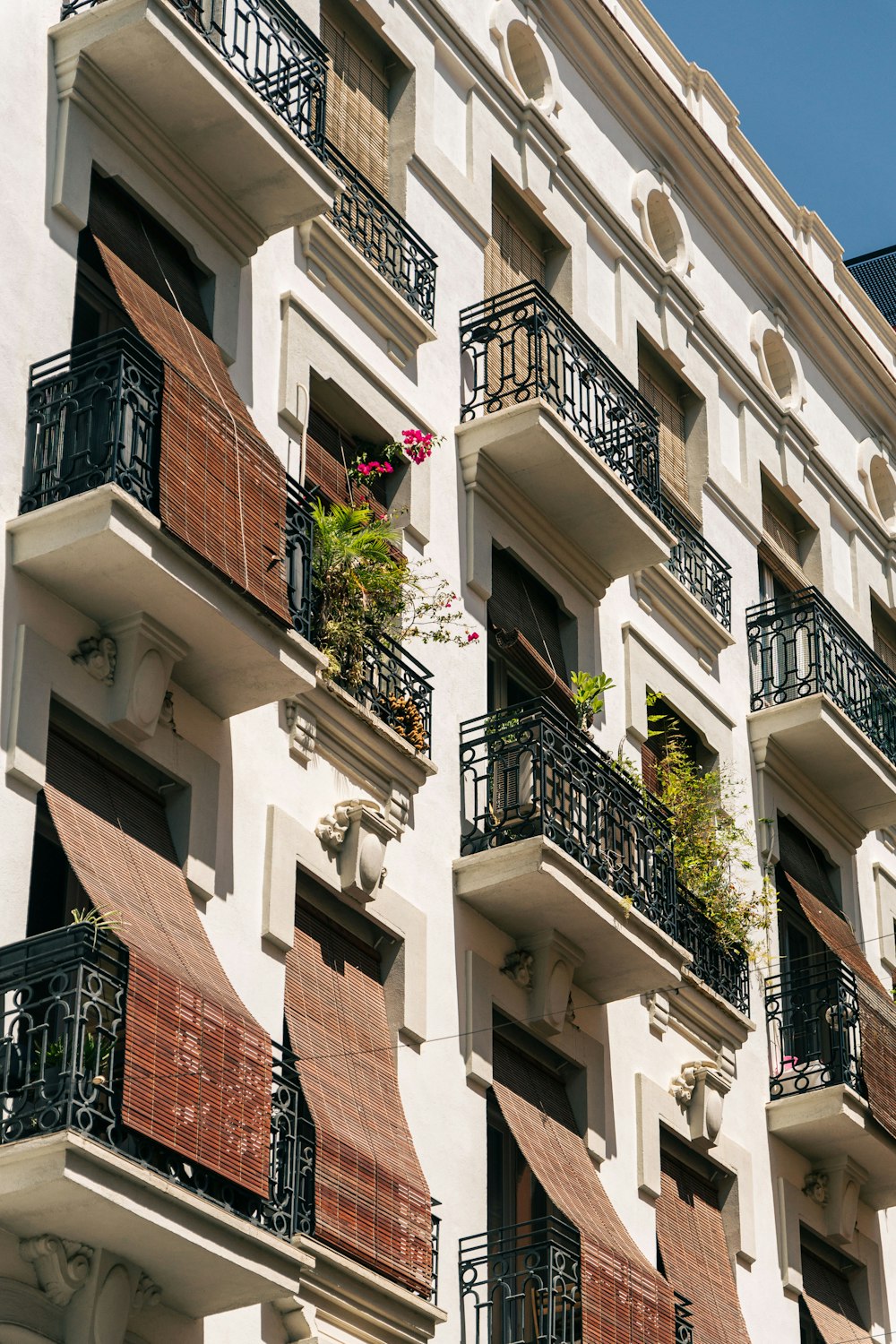 a tall white building with balconies and flowers on the balconies