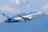 A passenger airplane with the WestJet logo is flying in the sky. The backdrop includes a range of blue mountains and a partly cloudy sky.