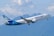 A passenger airplane with the WestJet logo is flying in the sky. The backdrop includes a range of blue mountains and a partly cloudy sky.