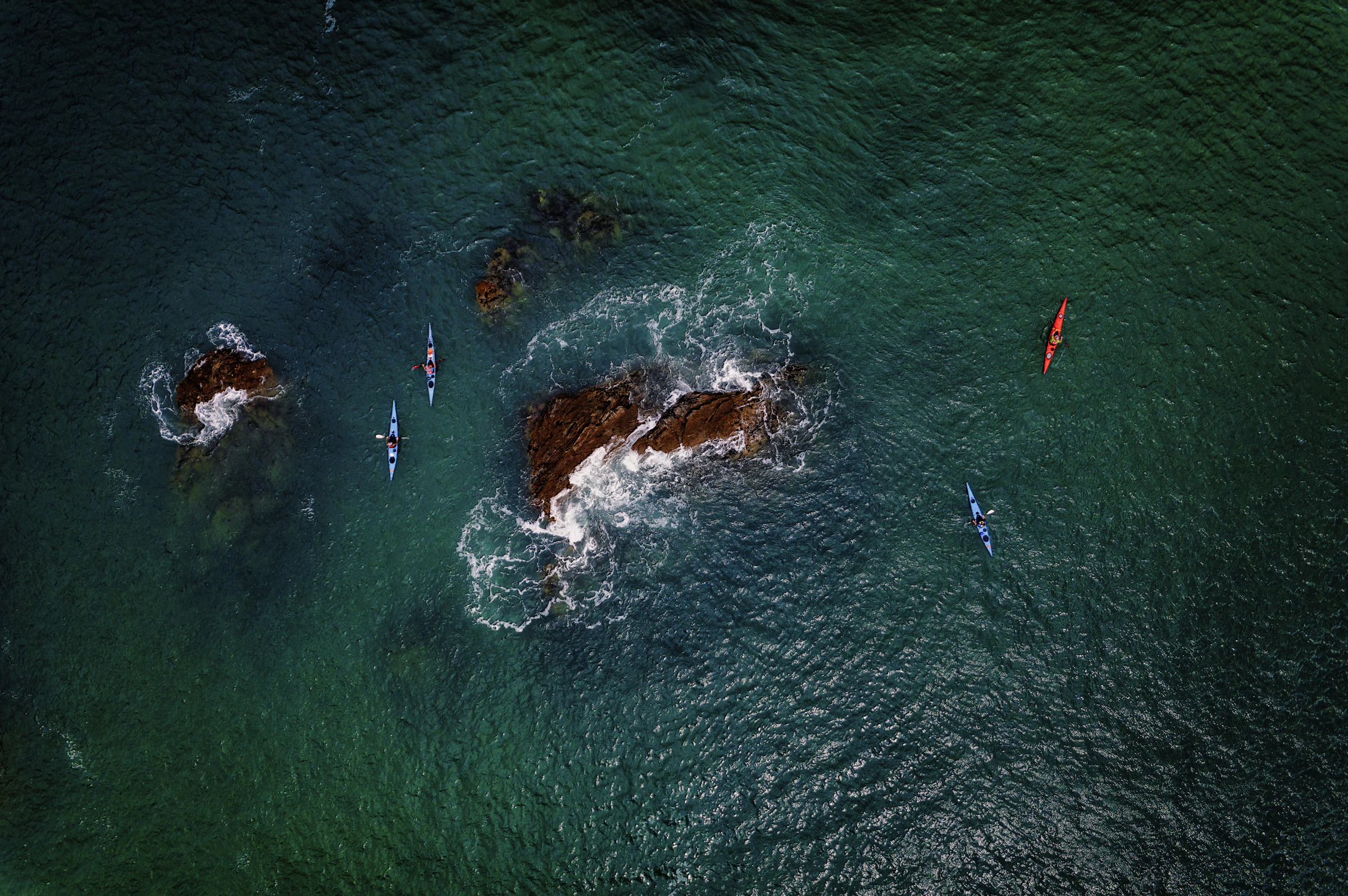 Kayakers navigating clear coastal water beside rocky formations