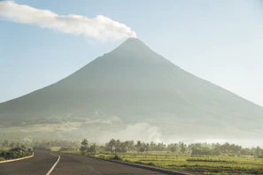 A smiling tour guide welcoming visitors with the majestic Rinjani volcano in the distance