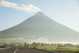 A smiling tour guide welcoming visitors with the majestic Rinjani volcano in the distance