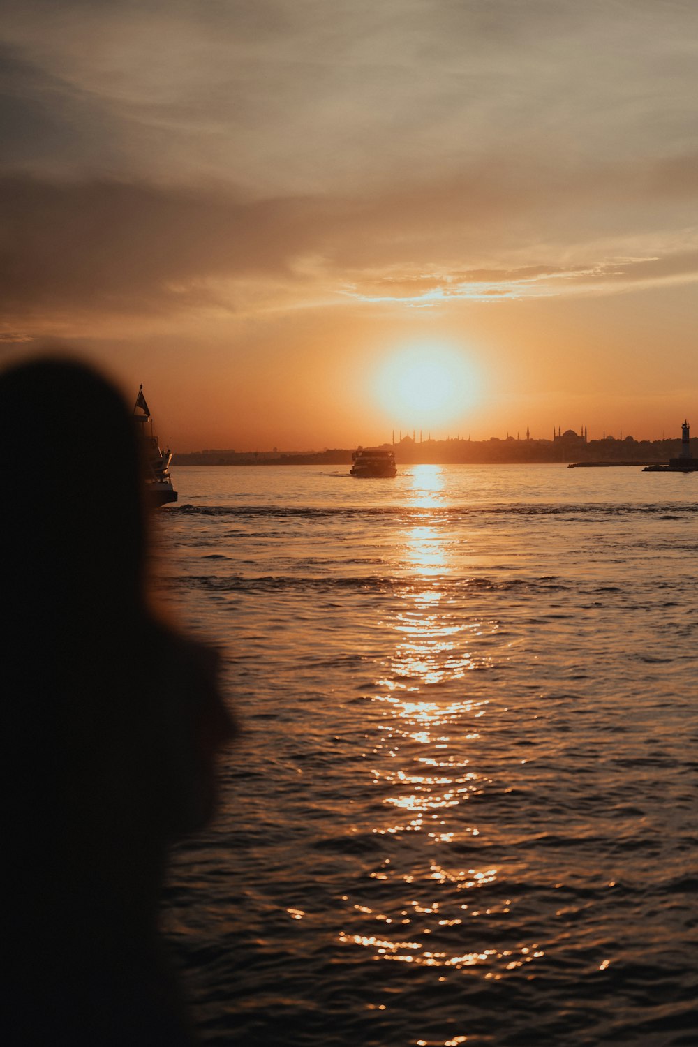 a person standing in front of a body of water at sunset