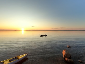 A serene lake at sunset with a kayak gently floating near the shore.