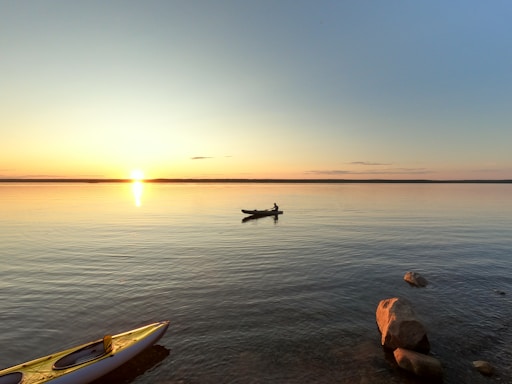 A serene lake at sunset with a kayak gently floating near the shore.