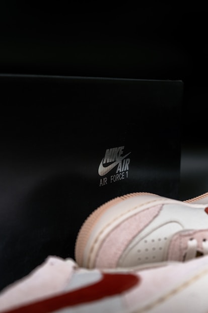 A pair of Nike Air Force 1 sneakers is displayed prominently against a dark background. The sneakers feature a light color scheme with a prominent swoosh logo, and the Nike Air Force 1 branding is visible in the background.