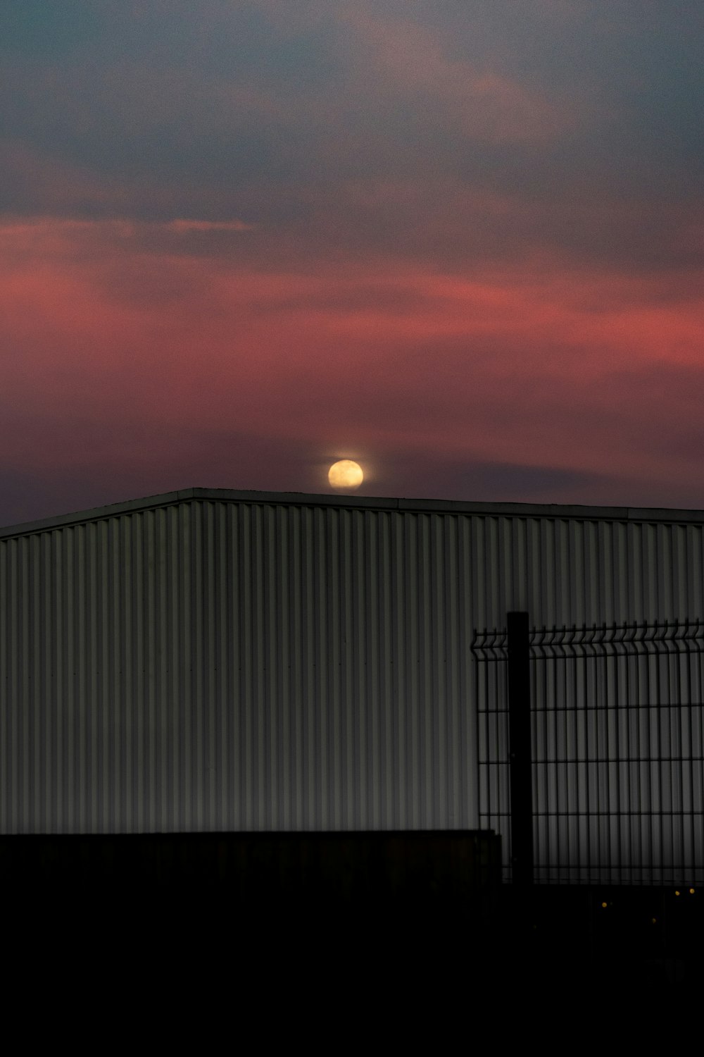 the sun is setting behind a building with a fence