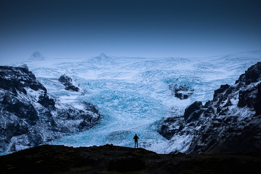 a man standing on top of a mountain next to a glacier