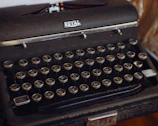 A vintage typewriter with circular keys arranged in the traditional QWERTY layout. The machine is predominantly black with a metallic finish, displaying a 'Royal' branding at the top. The keys have white lettering and numbers.
