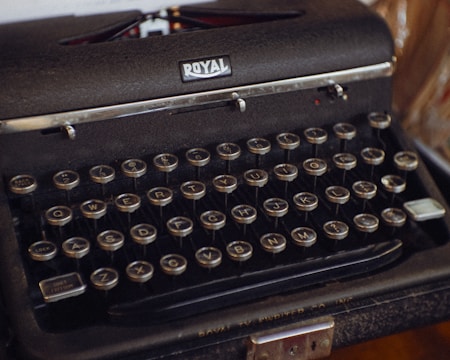 A vintage typewriter with circular keys arranged in the traditional QWERTY layout. The machine is predominantly black with a metallic finish, displaying a 'Royal' branding at the top. The keys have white lettering and numbers.