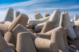 A collection of large, concrete tetrahedral structures stacked on top of each other under a clear blue sky. These structures are typically used as breakwaters in coastal areas to prevent erosion by absorbing wave energy.
