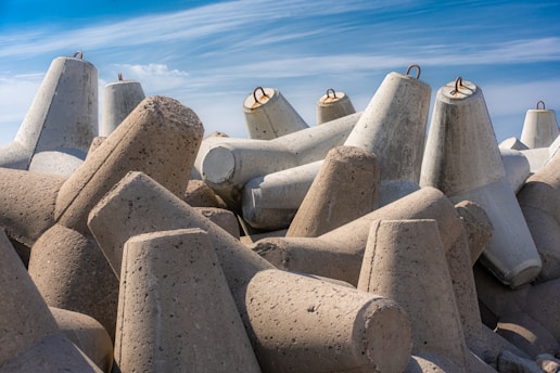 A collection of large, concrete tetrahedral structures stacked on top of each other under a clear blue sky. These structures are typically used as breakwaters in coastal areas to prevent erosion by absorbing wave energy.