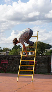 A friendly technician holding a ladder beside a clean gutter on a sunny day.
