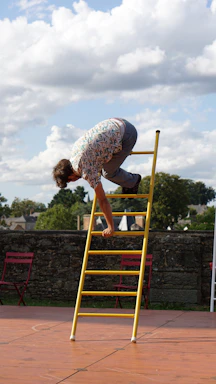 A friendly technician holding a ladder beside a clean gutter on a sunny day.