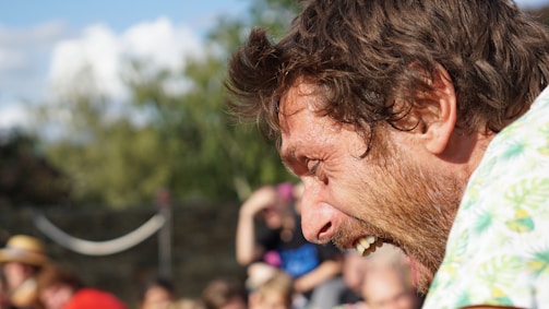 A candid portrait of a person laughing outdoors with blurred greenery in the background.