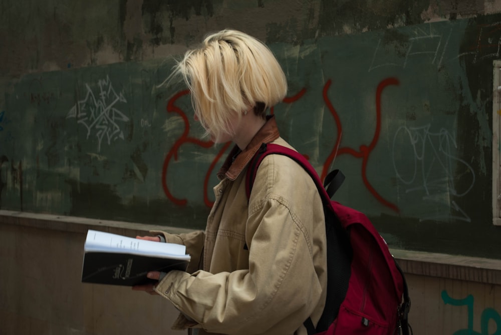 a woman with blonde hair and a backpack is reading a book