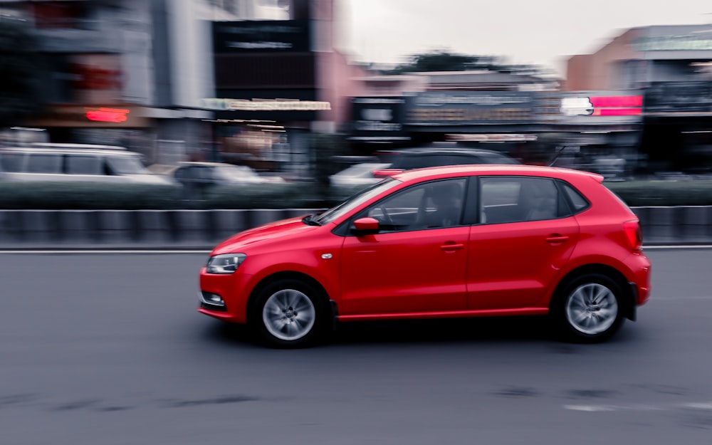 a red car driving down a street next to tall buildings