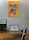 A modern office corner featuring a desk with a laptop and several colorful art prints hanging above.