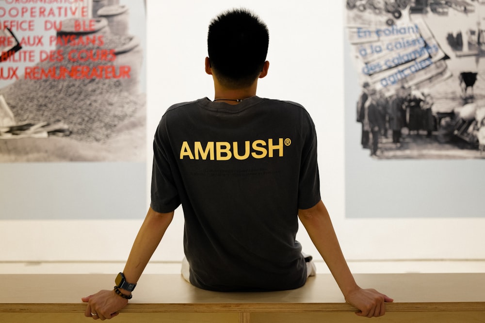 a man sitting on a bench in front of a wall with pictures on it