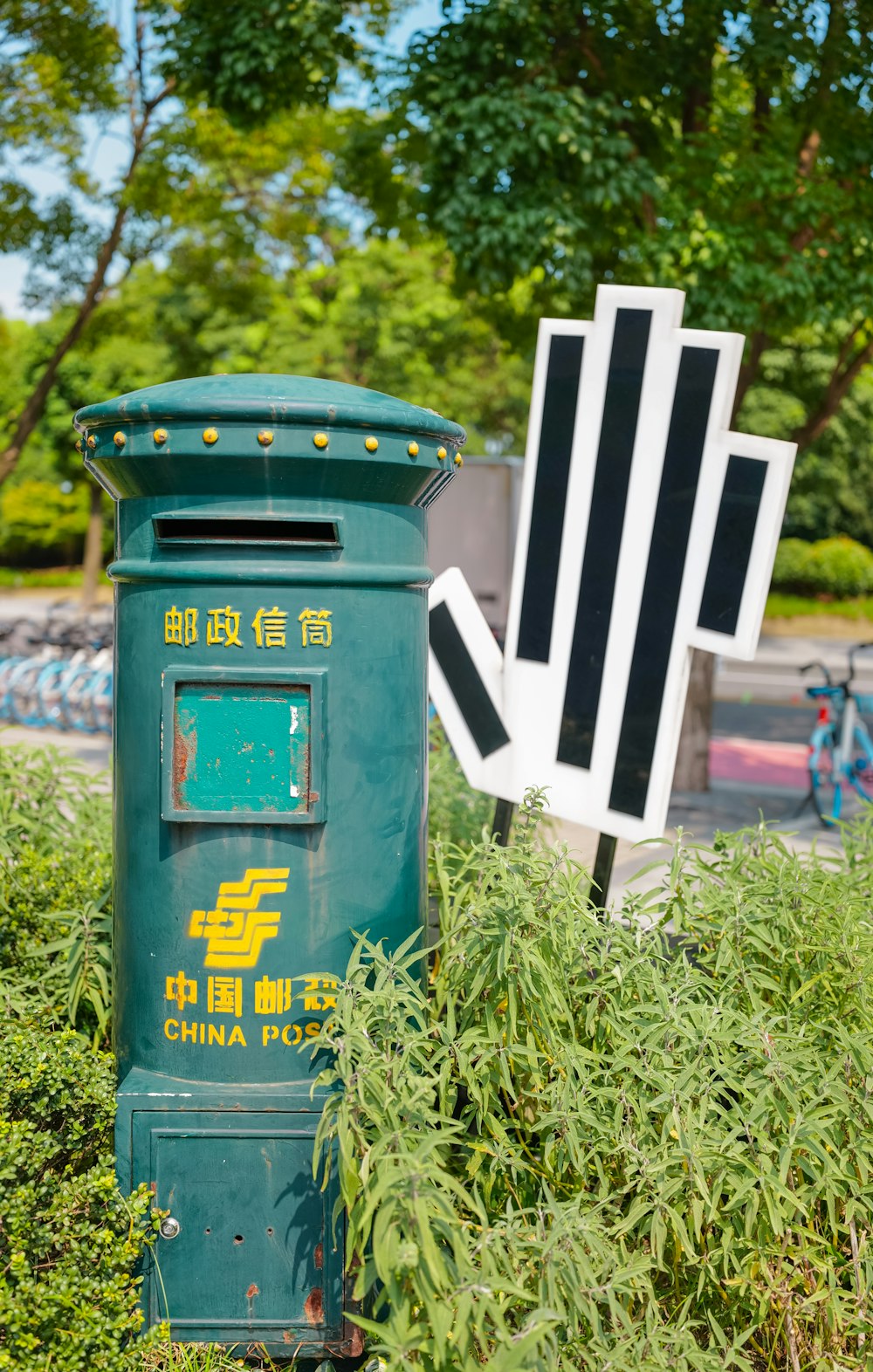 a green mail box sitting in the middle of a lush green field