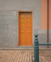 A freshly painted bright orange front door contrasting with a light gray house exterior under clear skies.