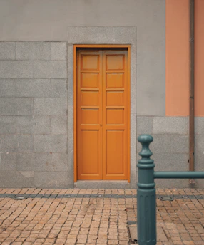 A freshly painted bright orange front door contrasting with a light gray house exterior under clear skies.