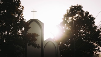 A radiant sunrise over a peaceful church with a cross silhouetted against the sky.