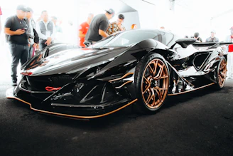 A sleek black supercar with gold accents parked under cinematic lighting, casting dramatic shadows on a glossy floor.