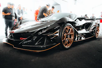 A sleek black supercar with gold accents gleaming under cinematic lighting on a dark glossy floor.