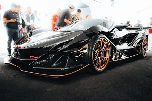 A sleek black supercar with gold accents gleaming under cinematic lighting on a dark glossy floor.
