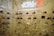 A display wall features a collection of baseball caps and sneakers arranged on transparent shelves against a marble backdrop. The caps exhibit various team logos, while the sneakers include different styles and colorations. A neon sign above the display reads 'Powered by Miki Guerra of Mag Park.'