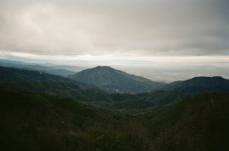 A panoramic view from a mountain summit overlooking rolling green hills.