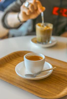 A hand gently placing a handcrafted wooden stirrer into a steaming cup of coffee on a marble countertop.