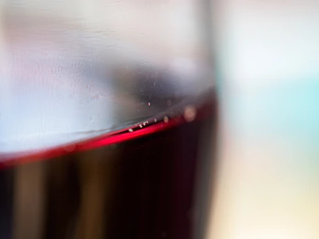 Close-up of a wine glass filled with deep red Greek wine against a white tablecloth.