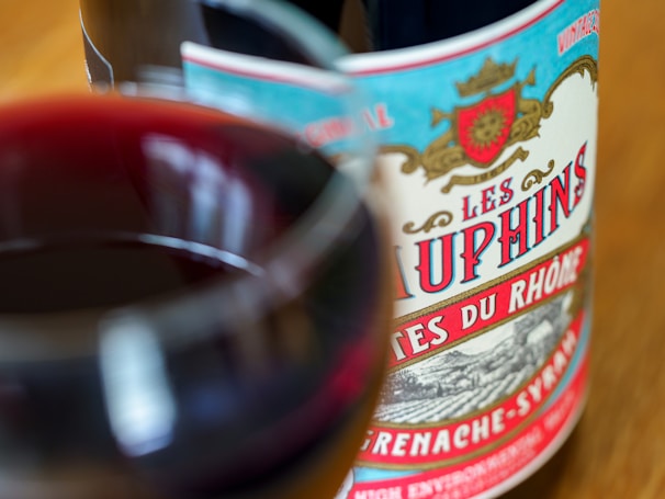 Close-up of a glass of red wine beside a bottle labeled Côtes du Rhône on a stone surface