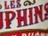 Close-up view of stylized text with bold, vivid red and blue letters outlined in black against a beige textured background. The design includes ornamental scrolls in gold, adding a vintage or classic feel.