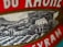 A close-up of a label featuring a detailed illustration of a vineyard hillside with several small buildings. The label includes bold red text with serif fonts.